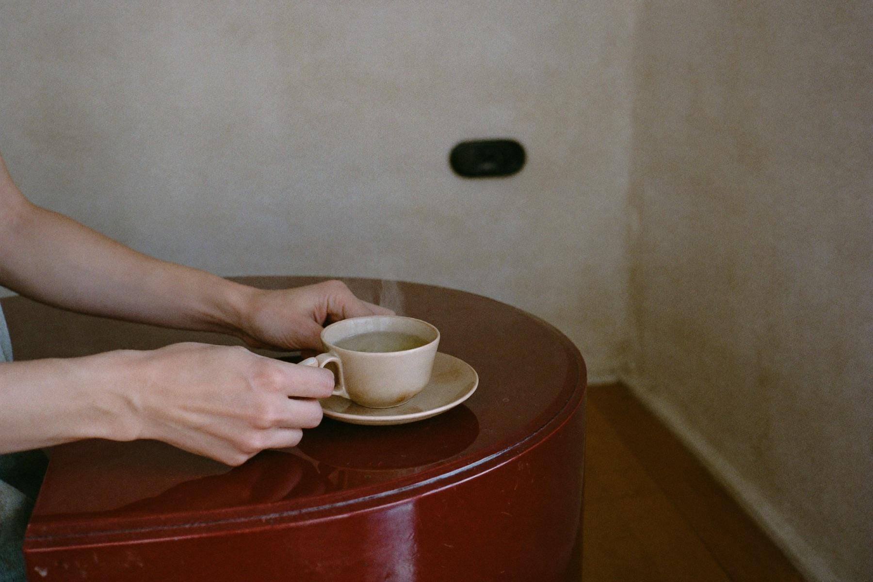 A ceramic cup of herbal infusion passed across the burgundy reception counter