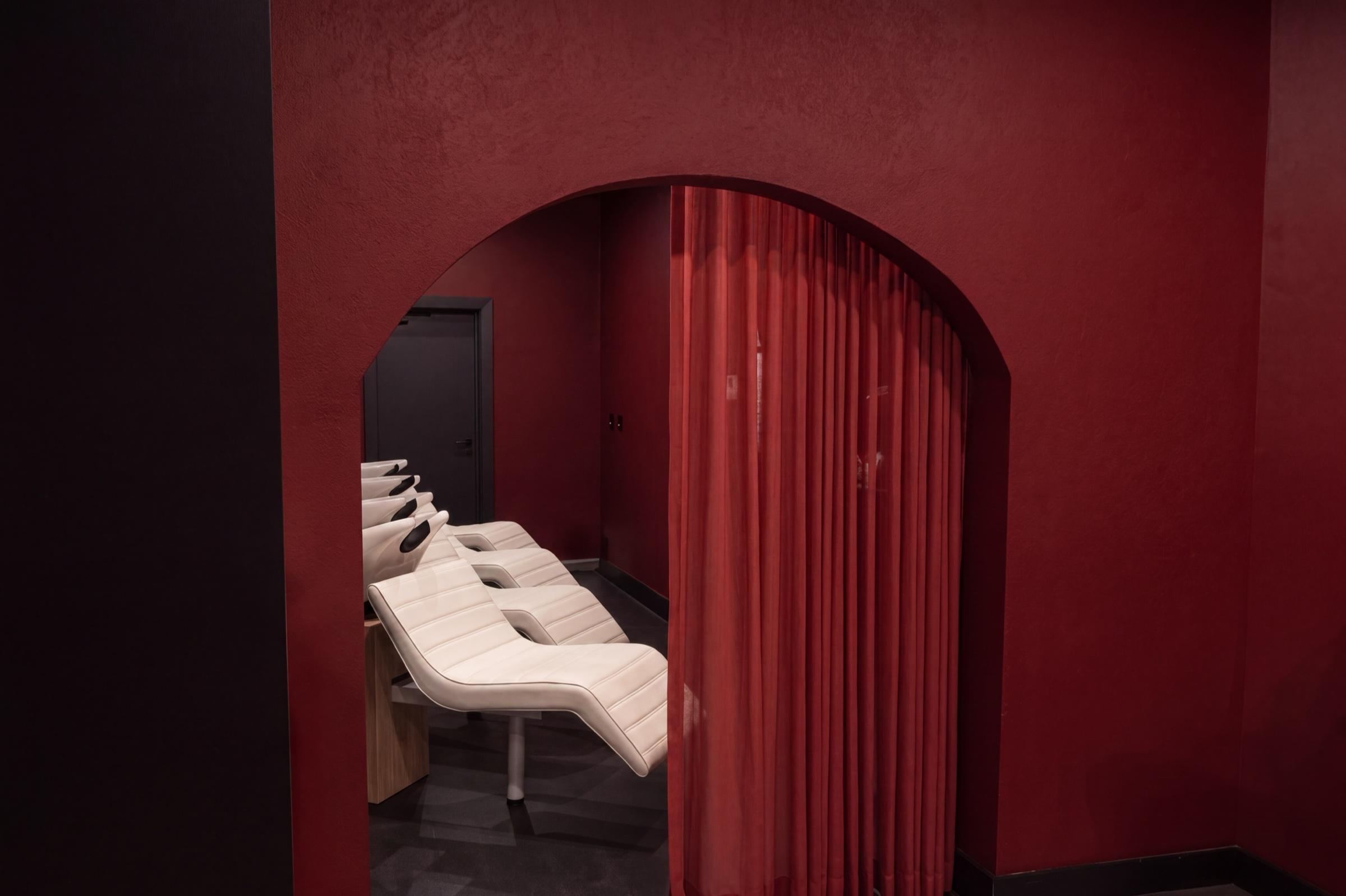 The red arch of the wash sanctuary, sheer curtain drawn aside, seen from the salon floor