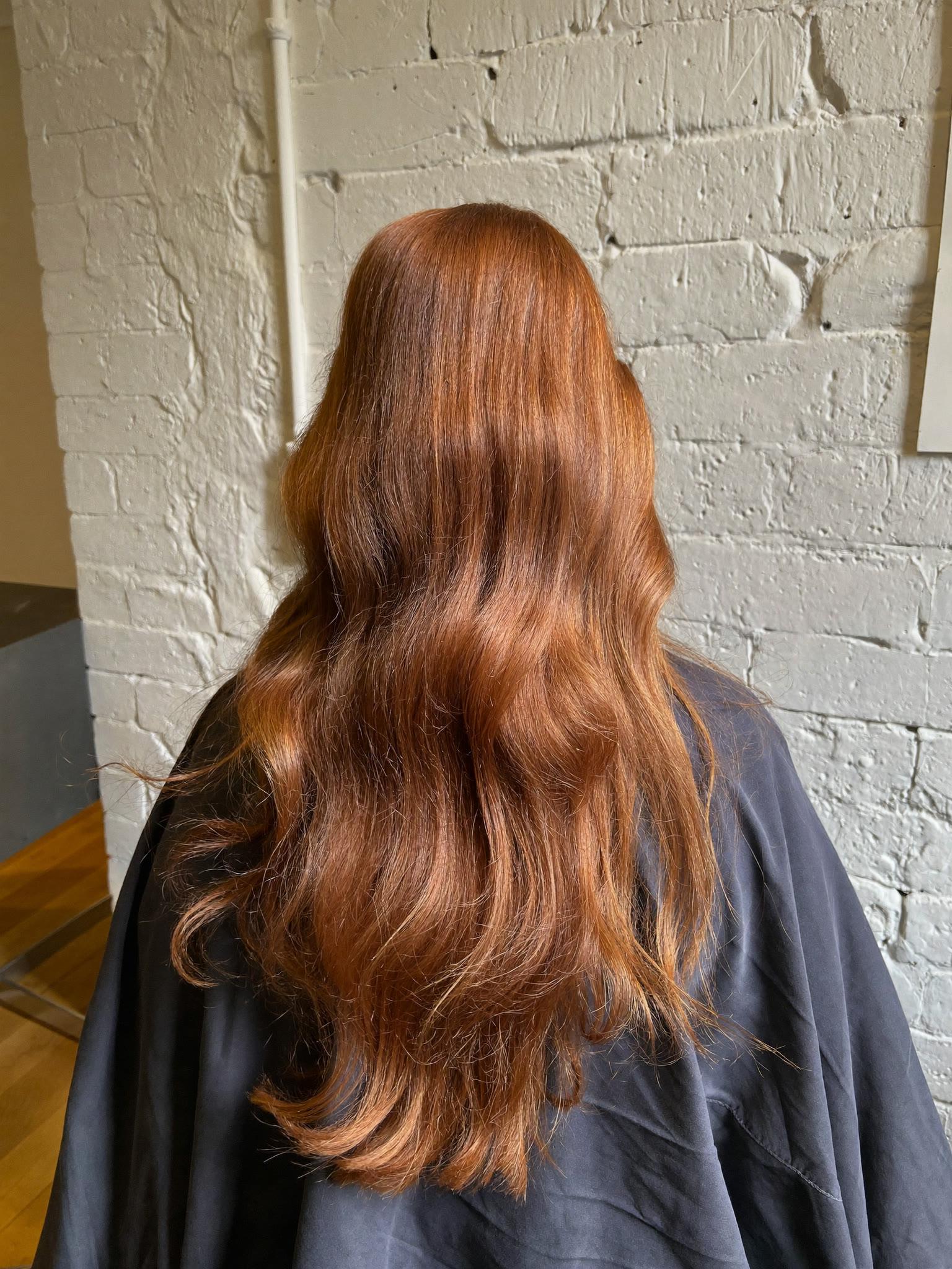 Dimensional copper hair colour falling over a charcoal smock in window light
