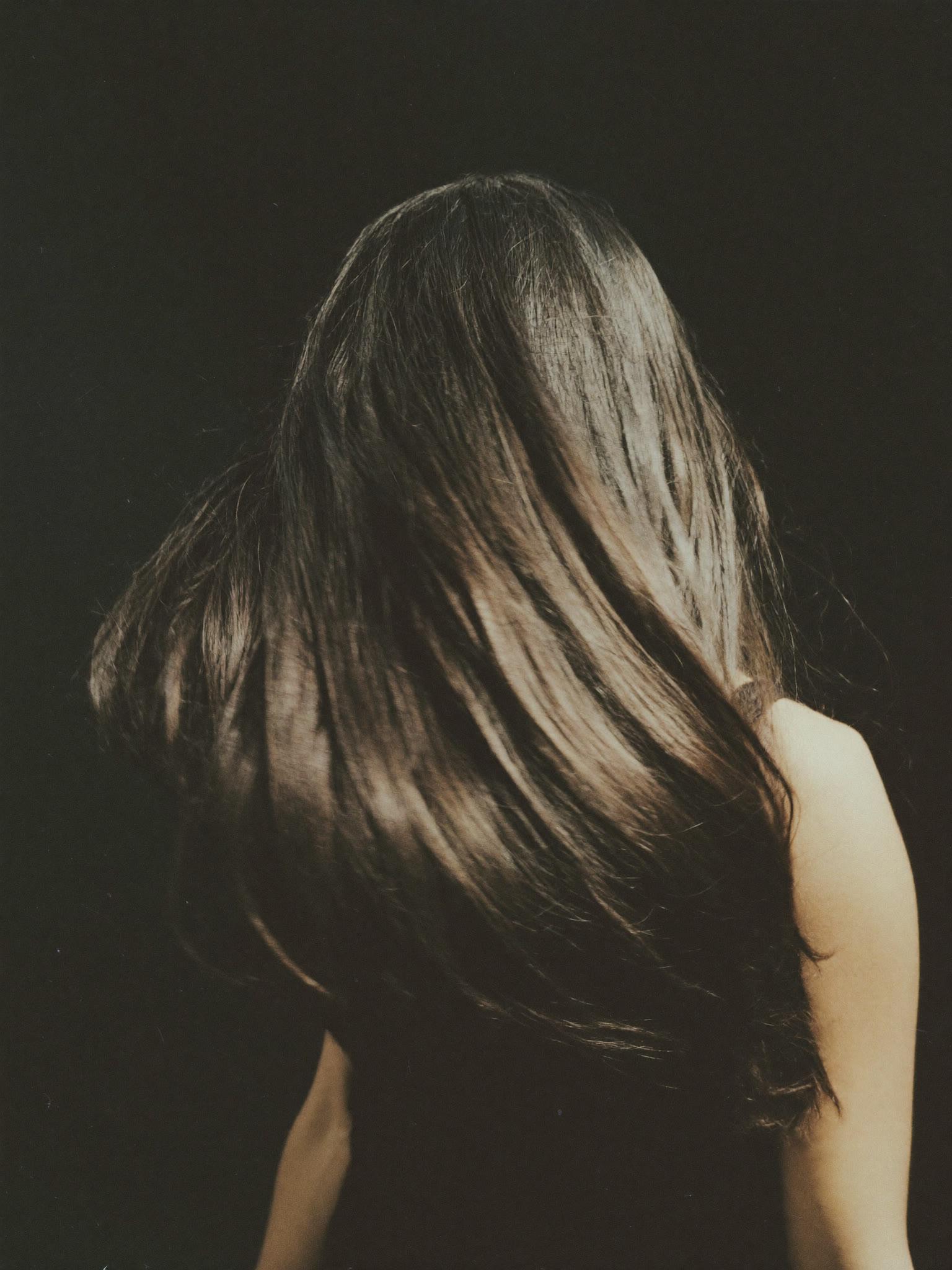 Long dark hair fanning mid-turn against a charcoal backdrop